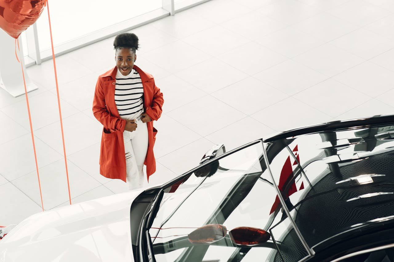 Cheerful woman in red coat exploring a new car at a dealership. Excited car shopping experience.